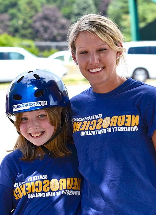 A U N E student stands with a kid wearing a bike helmet for a neuroscience outreach program